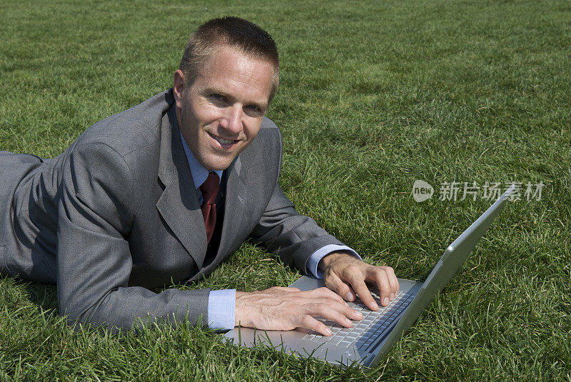 微笑的商人草地上的笔记本电脑