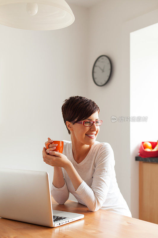 年轻漂亮的女人在厨房用笔记本电脑喝咖啡