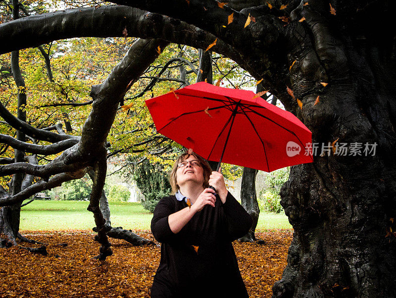 女人撑着红伞走过秋叶