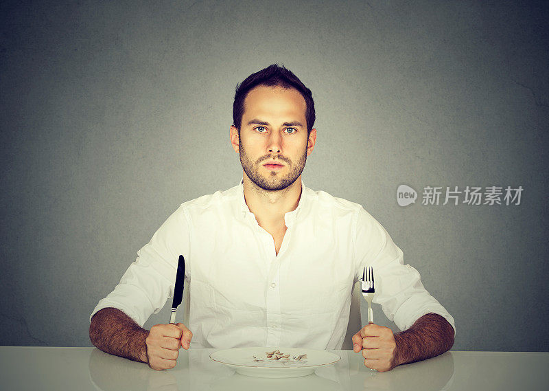 拿着刀叉的男人坐在空盘子的桌子旁
