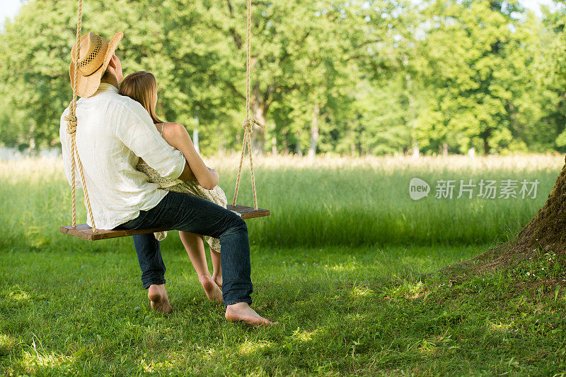 一对浪漫的年轻夫妇坐在森林里的秋千上