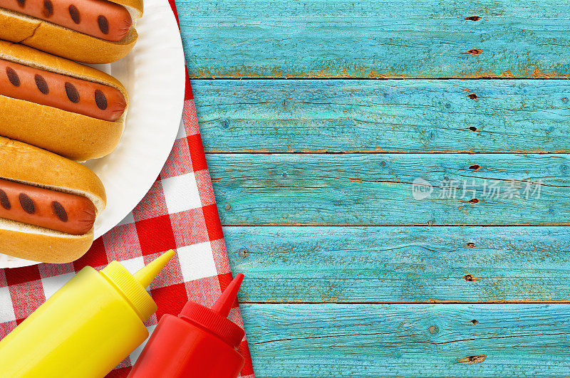 烤热狗，纸盘子，番茄酱，芥末瓶子，野餐桌上