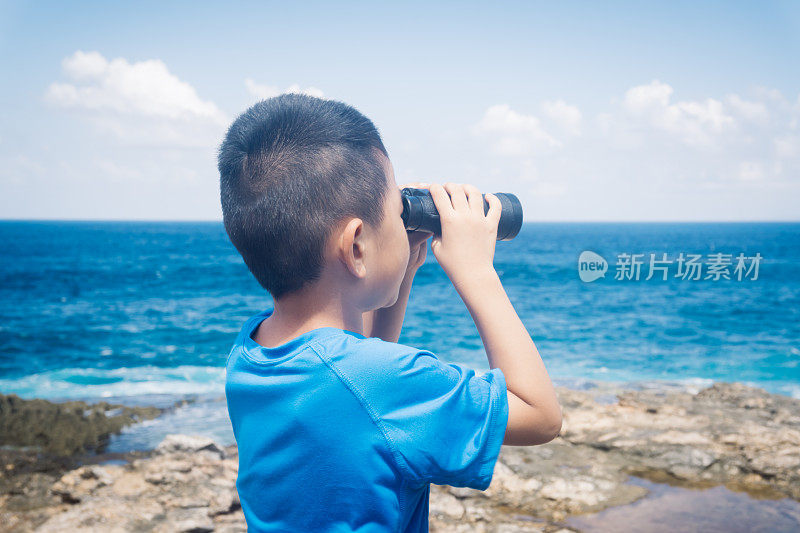 小男孩在悬崖上用双筒望远镜看