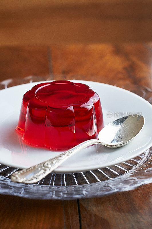 白色的盘子上放着红色的果冻，银色的勺子