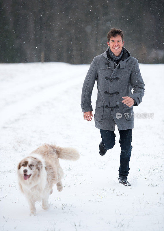 英俊的男人和他的狗在雪地里奔跑