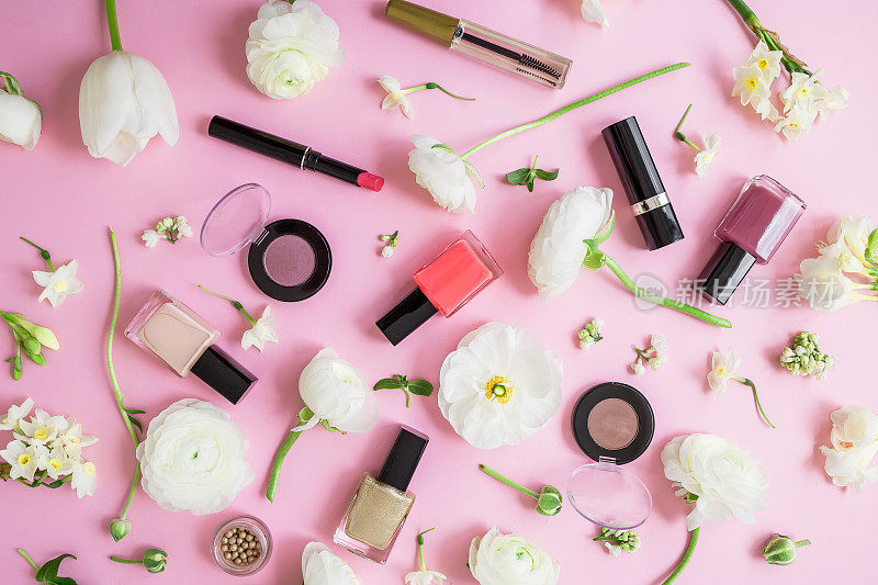 女性的办公桌上有化妆品，口红，指甲油，眼影和白色的花朵孤立在粉红色的背景。平躺，俯视图。