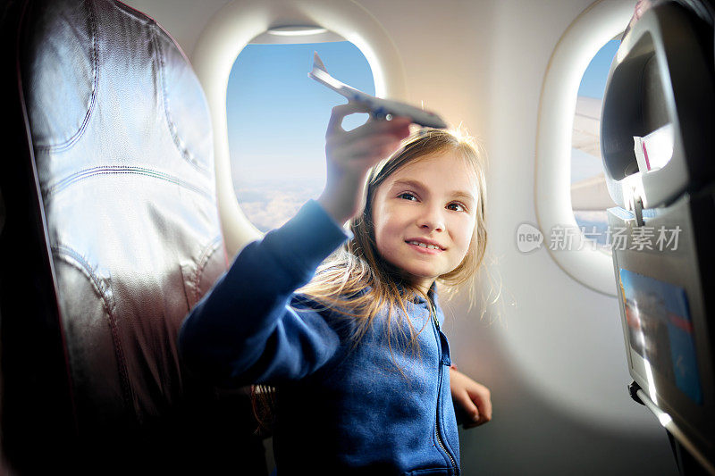 可爱的小女孩乘飞机旅行。孩子坐在窗边玩玩具飞机。