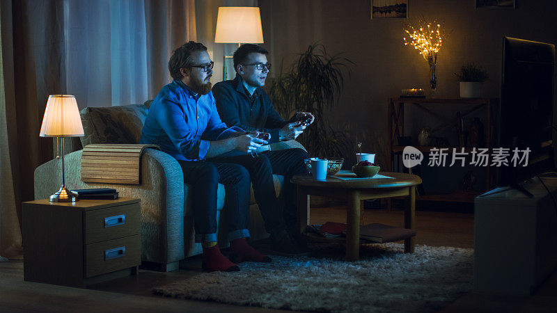 晚上两个朋友坐在客厅的沙发上玩电子竞技游戏。他们互相推搡，很友好。