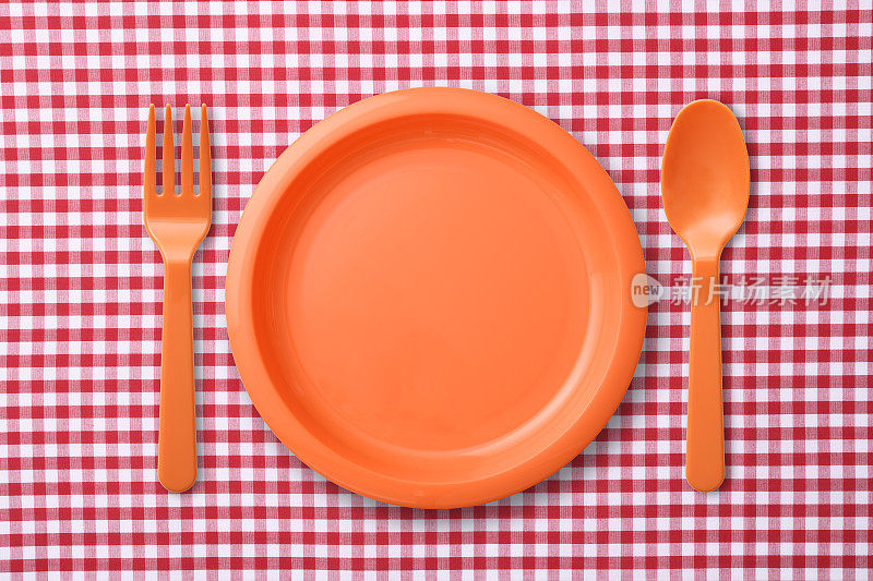 红色格子布桌布上的橙色塑料盘子和勺子