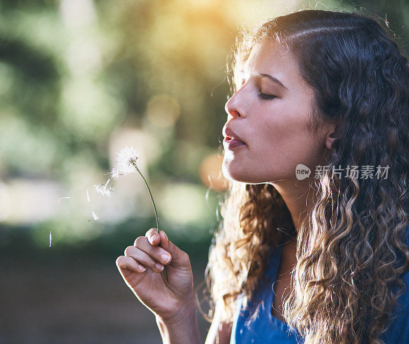 美丽的女孩吹落蒲公英的种子