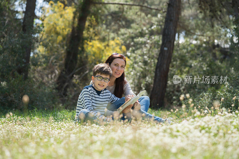 美丽的女人和她的儿子坐在森林里看书