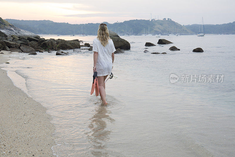 女人带着潜水装备漫步在海滩上