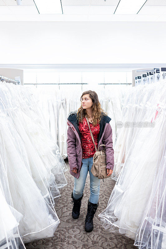 年轻女子在精品折扣店的过道里购买婚纱礼服，许多白色服装挂在衣架排上
