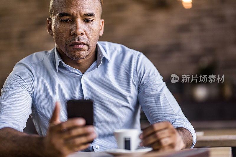 严肃的非裔美国商人在咖啡馆用手机。