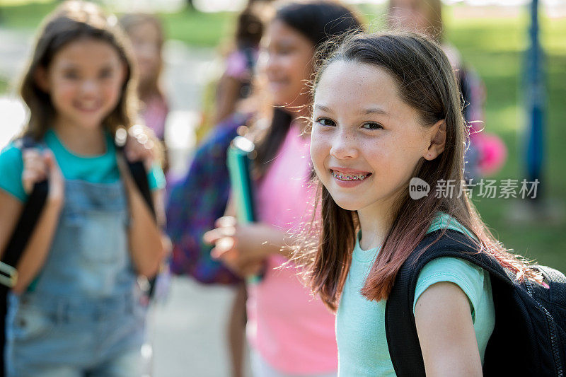一个小女孩站在不同的同学群中，对着镜头微笑。