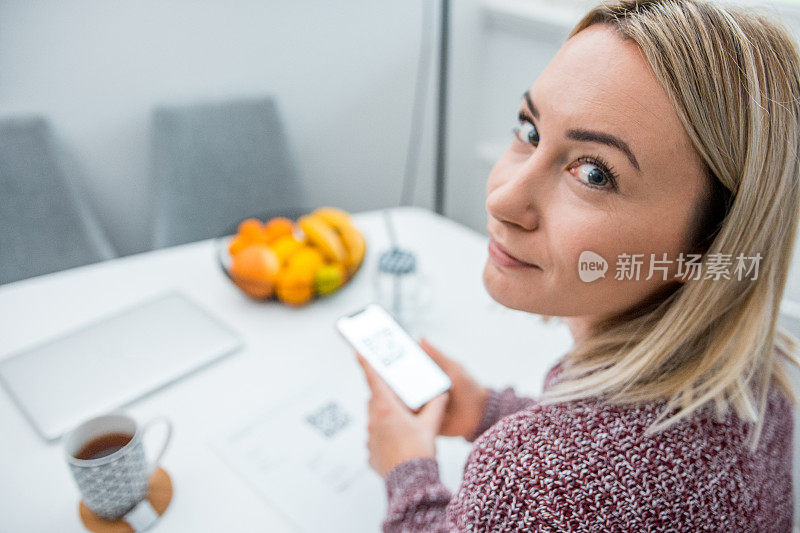 一名女子在厨房用智能手机扫描账单上的二维码