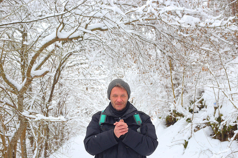 美丽微笑的成年男子徒步旅行者戴着针织帽徒步雪山森林的肖像