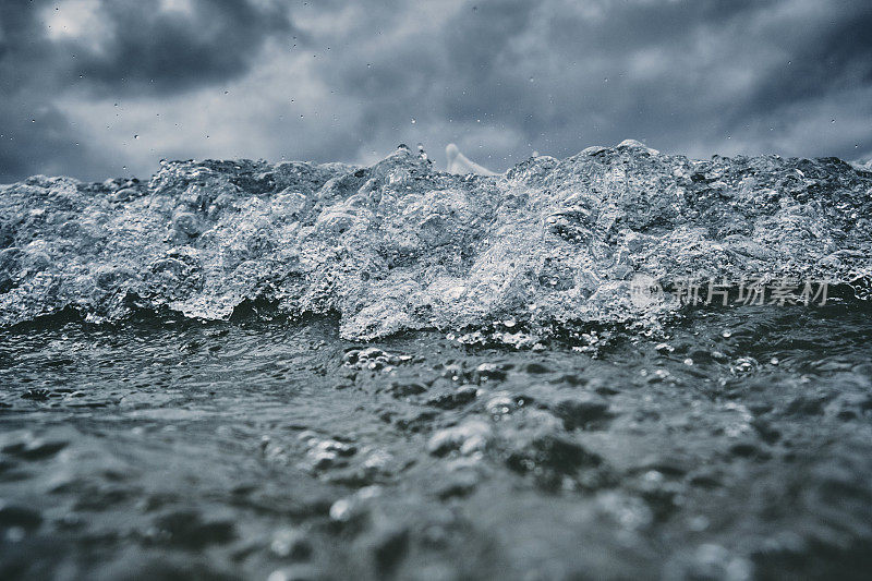 破碎的波浪接近相机在海面上与一个黑暗戏剧性的暴风雨天空。