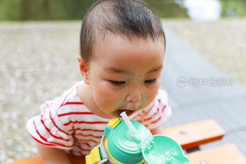 这是一个中国小女孩在户外试图从瓶子里喝水的特写