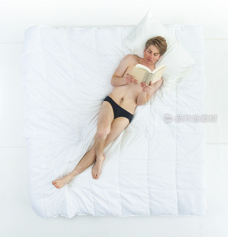 性感的男人在床上穿着内衣，看书