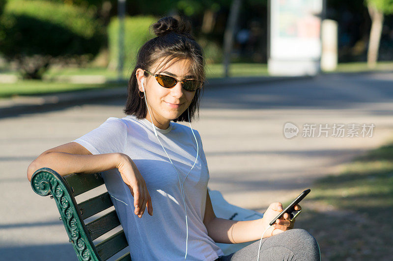 一个穿着运动服的年轻女子正在室外听手机里的音乐