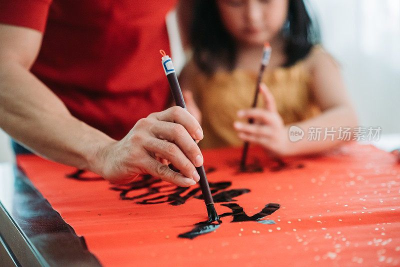 亚洲华人父亲和女儿在一起写中国书法在红彩纸在中国新年前夕