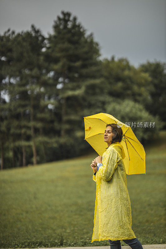 女人穿着雨衣，撑着雨伞，在雨天行走