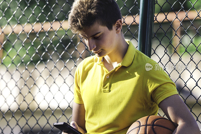 十几岁的男孩用智能手机发短信。十几岁的男孩拿着篮球