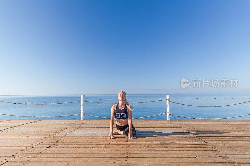 一个年轻女子在海边的木制码头上做瑜伽