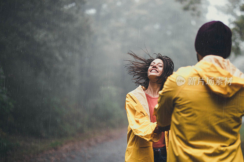 快乐的情侣在大自然中手牵着手，在雨中旋转。