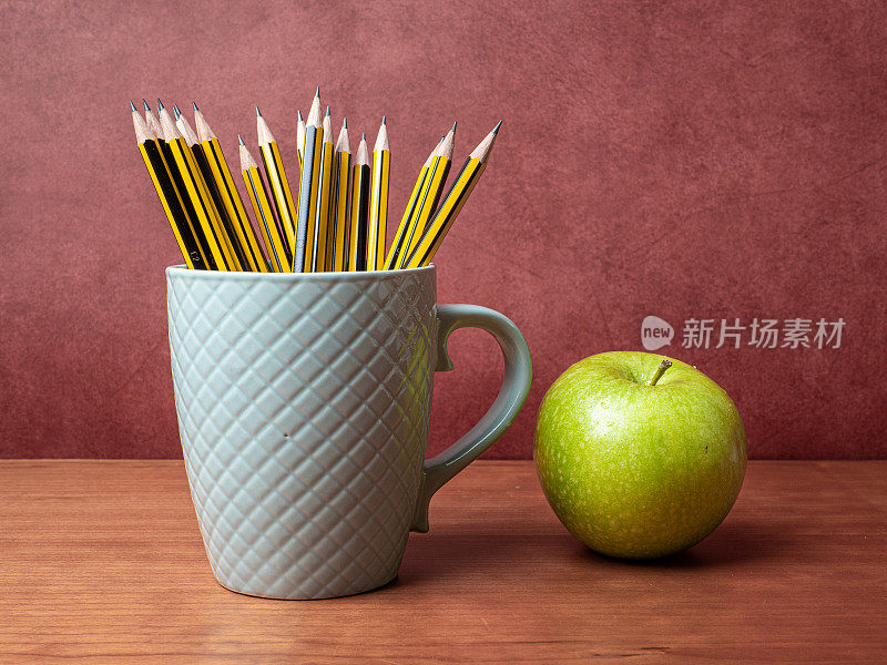 红色背景的木桌上放着苹果和铅笔盒