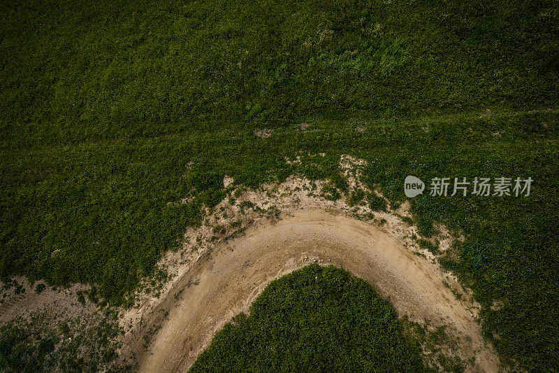 山地车道蜿蜒穿过开阔的绿色草地的鸟瞰图