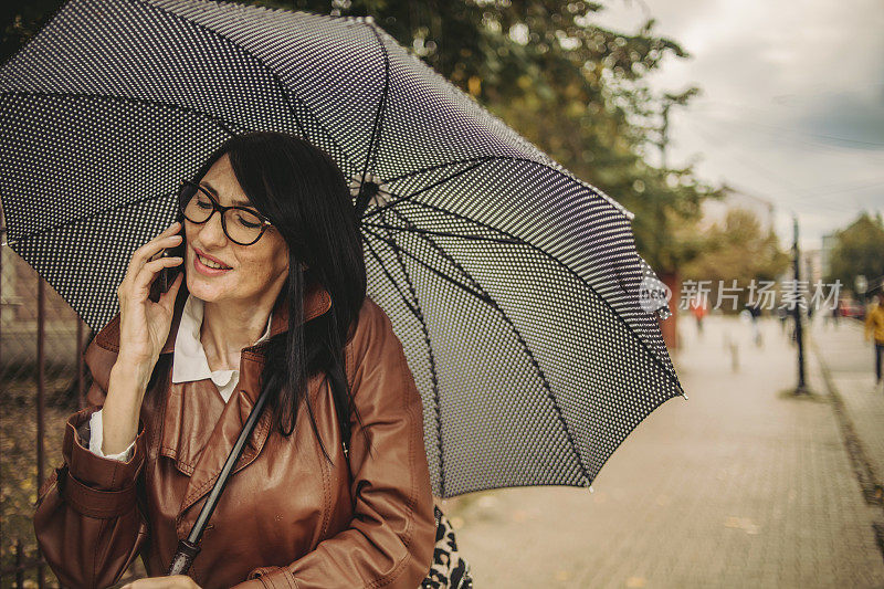 一位漂亮的商务老妇人在雨中行走，手里拿着手机