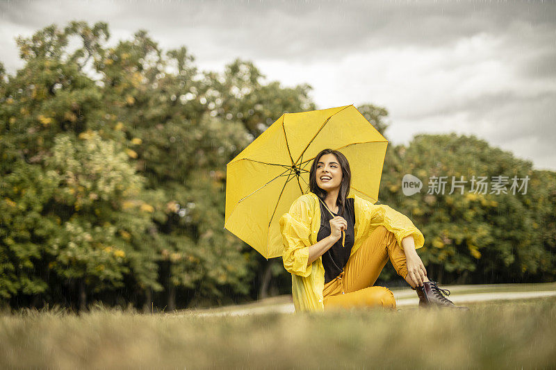 美丽的年轻女子穿着黄色雨衣，拿着黄色雨伞在户外