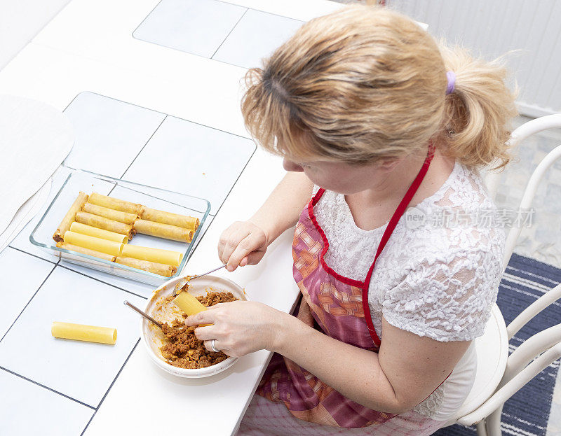 这个女人正在准备食物，意大利面卷。女人，白人，在家做饭。俯视图