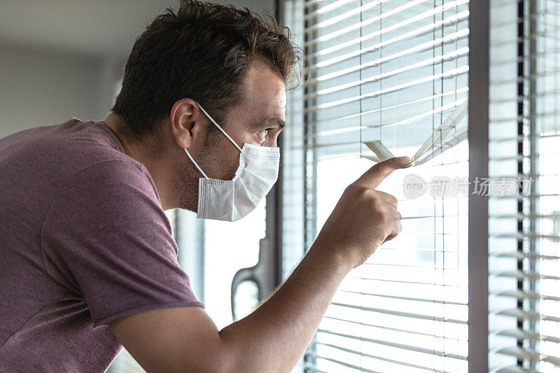 一名男子在医院隔离期间从百叶窗后张望。冠状病毒检疫隔离场景