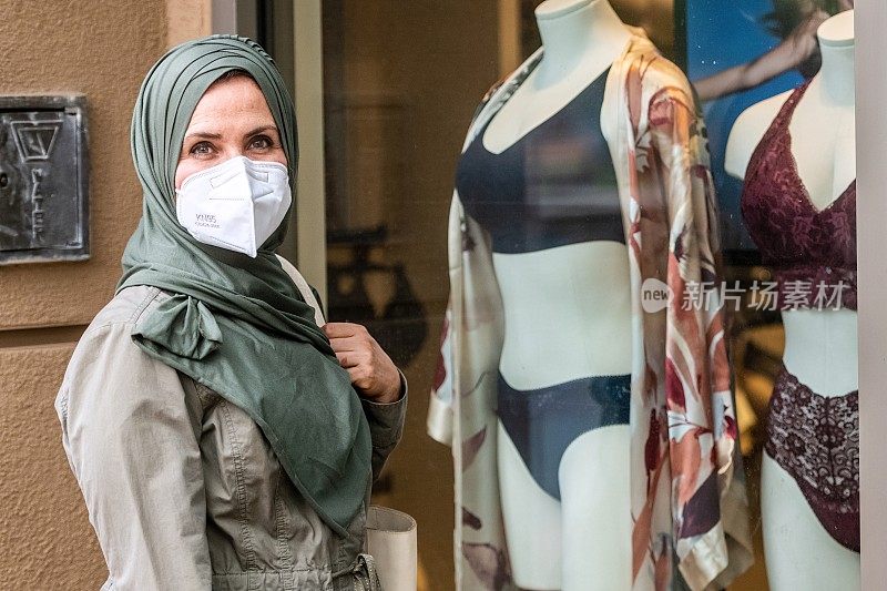 成熟的白人穆斯林妇女穿着n95保护面罩在橱窗里购物