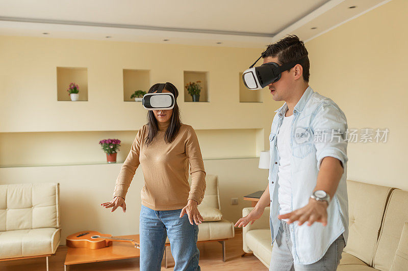 英俊的年轻人和他的亚洲女友正在玩视频游戏使用虚拟现实模拟器。