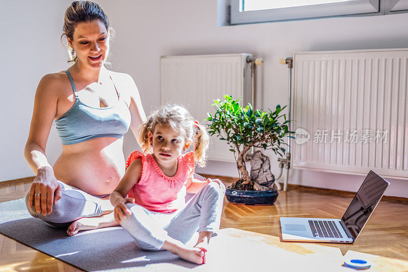 怀孕母亲在家和女儿练习瑜伽