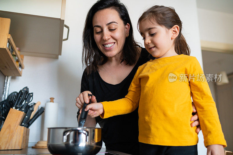 妈妈在帮她的小女儿做饭，她在厨房里拌汤