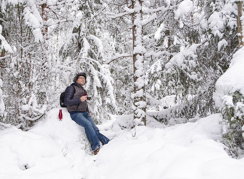 一个男人在白雪覆盖的森林里喝咖啡。男,中年白种人。步行旅游。
