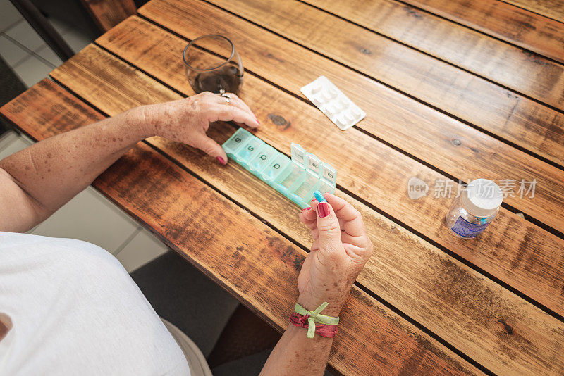 年长女性的手在取药片或把药片放进每日药片收纳器