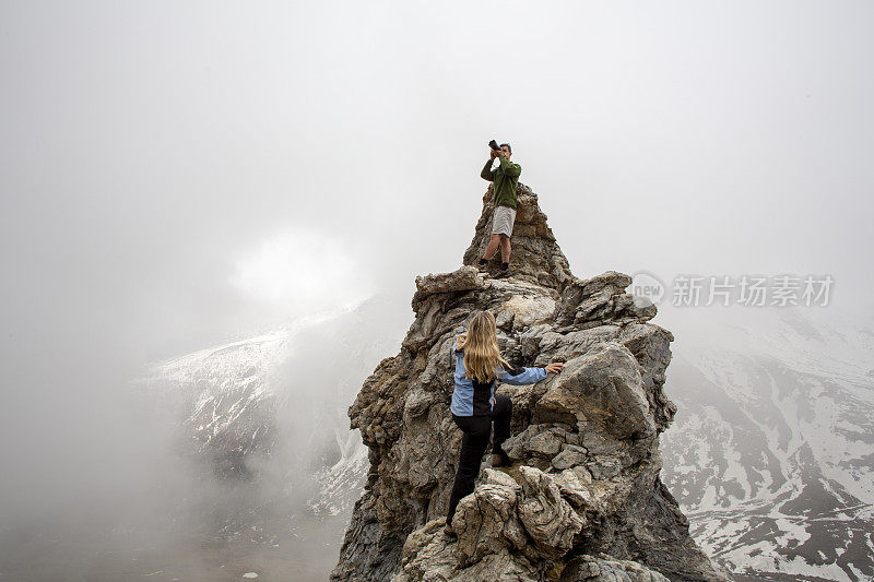 徒步旅行者在岩石顶峰休息，用相机拍照