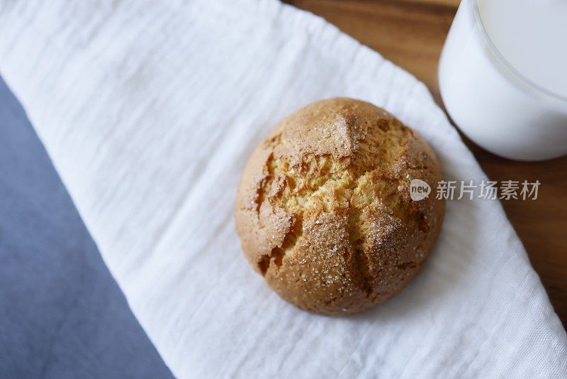 一个大的圆形橙色饼干和一杯牛奶在白色亚麻布餐巾上，在一个深灰色的石头背景，特写