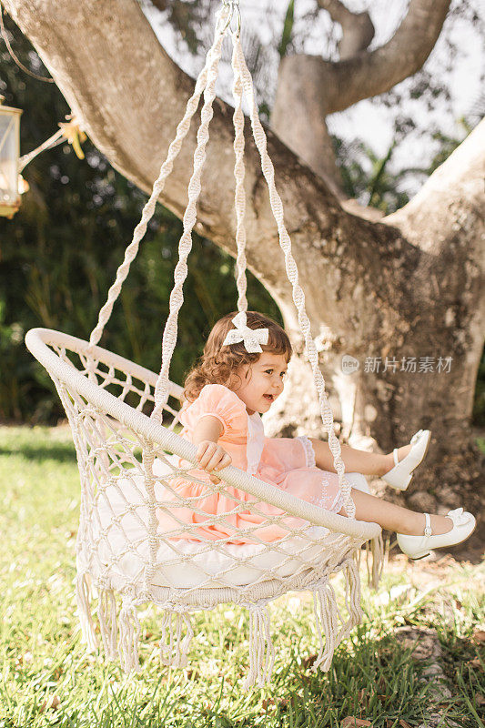2019冠状病毒病(COVID-19)期间，刚学走路的小女孩穿着复古的桃色连衣裙，坐在波西米亚树椅上，在家里过她简单的2岁生日