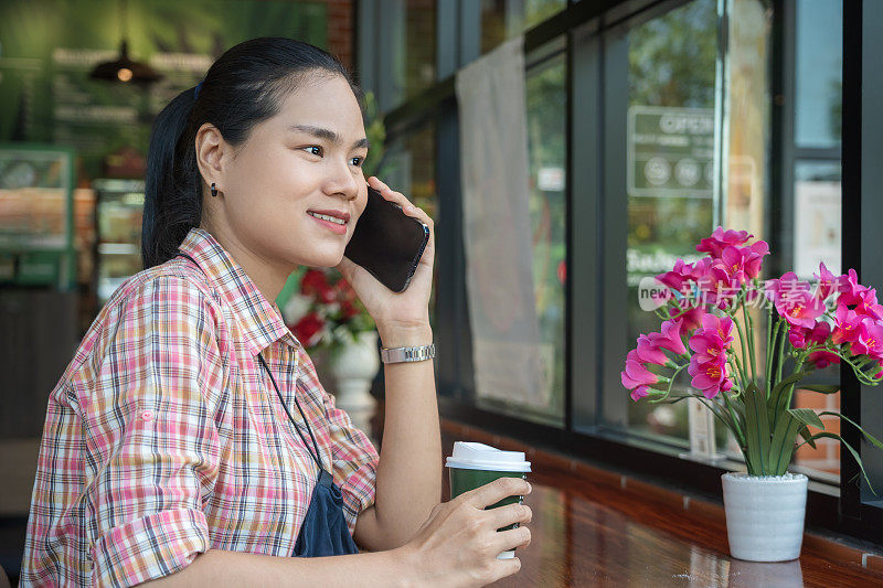 一个年轻迷人的女人独自坐在咖啡店里用手机打电话。迷人的女性微笑和打电话与手机。积极的情绪和生活方式的概念
