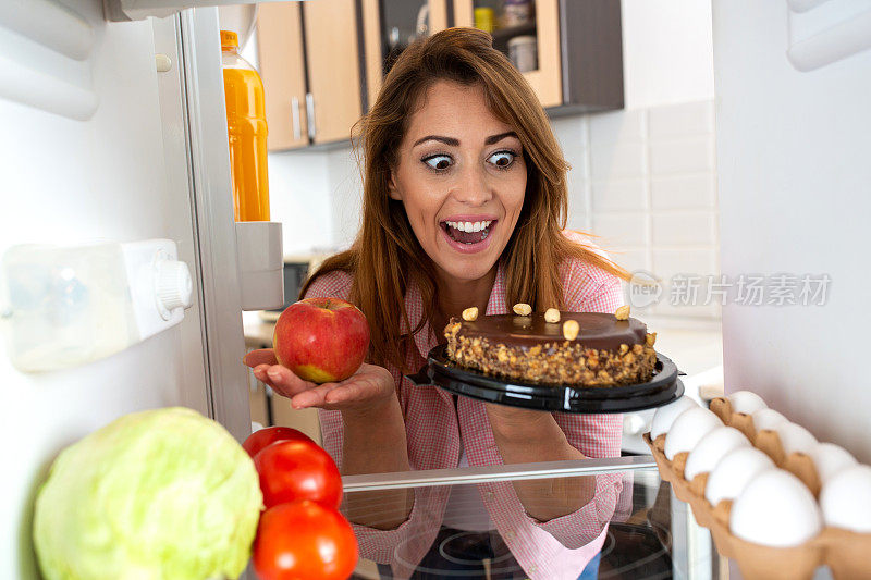 一个黑发的年轻女子在苹果和蛋糕之间选择