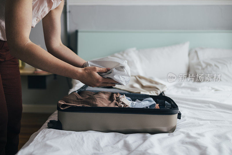 这是一张剪辑过的照片，照片上是一个白人妇女在卧室的床上收拾她的手提箱