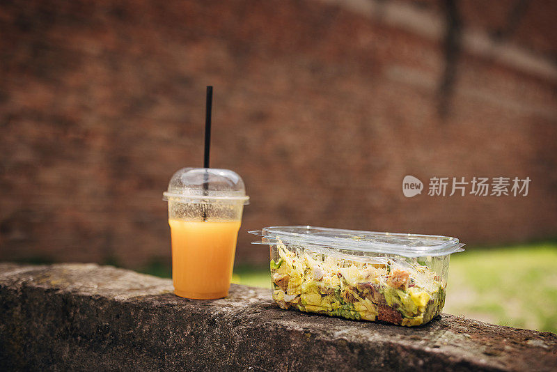 塑料杯装橙汁，吸管，塑料容器装健康沙拉