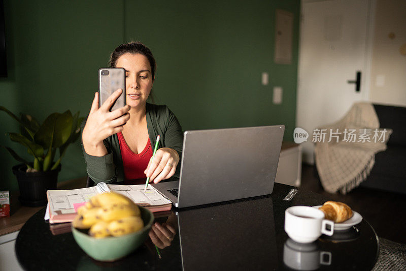 中年女性在家里用智能手机和笔记本电脑打虚拟商务电话